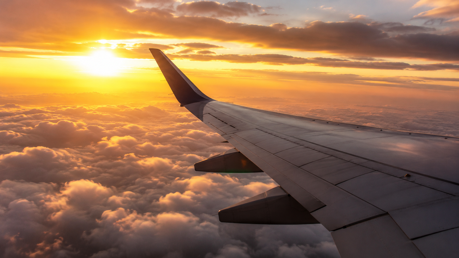 Airplane wing over clouds at sunset